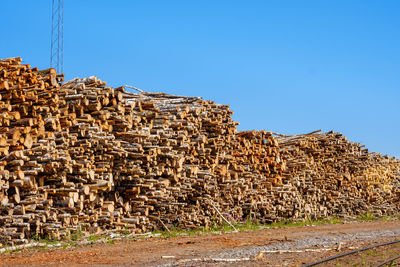 Stack of logs in forest against clear blue sky