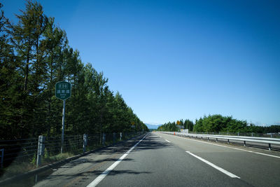 Road amidst trees against clear blue sky