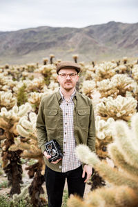 Young man with cap and vintage camera in cholla cactus field