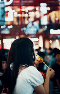 Rear view of woman eating food at night