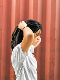 Side view of young woman standing against wall