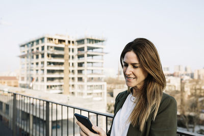 Portrait of smiling young woman standing on mobile phone in city