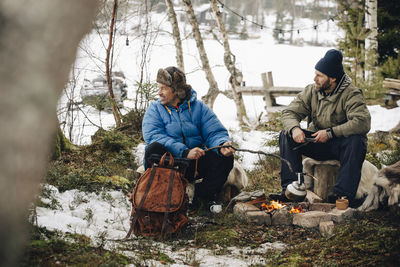 Mature man preparing tea while sitting with friend by campfire