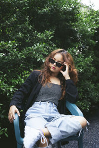 Young woman sitting on sunglasses against trees