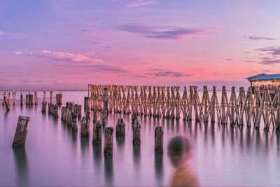 Wooden posts in sea against sky during sunset