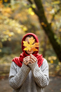 Woman covering face with autumn leaf