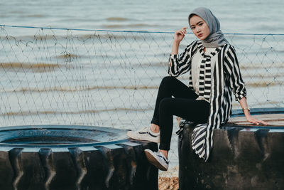 Woman with umbrella sitting against rippled water