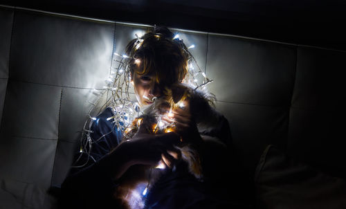 Portrait of teenage girl holding illuminated string lights in darkroom