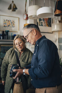 Senior male owner holding vase by female customer checking price tag at store