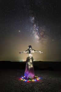 Rear view of woman with illuminated string lights standing on field against sky at night