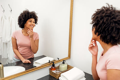Smiling young woman using phone while standing on mirror