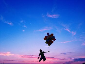 Person jumping with balloons at sunset