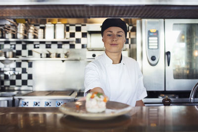Young female chef serving dish on counter at restaurant