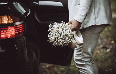 Midsection of man holding bouquet by car