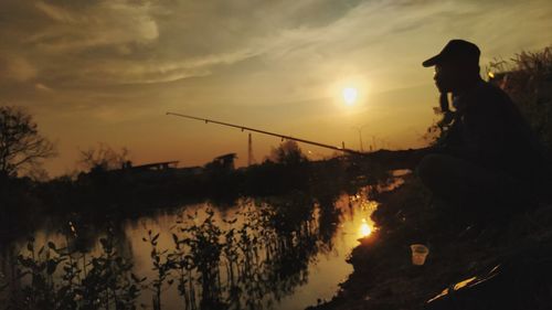 Silhouette man fishing in lake against sky during sunset