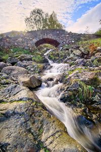 Stream flowing through rocks against sky