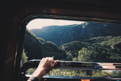 Cropped hand of woman holding window railing against mountain in bus
