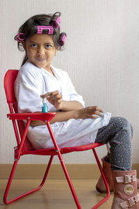 Portrait of girl applying nail polish while sitting on chair at home