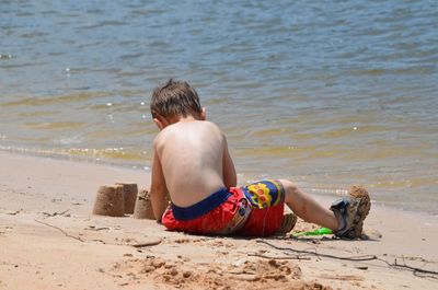 Rear view of boy sitting on shore at beach