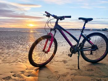 Bicycle on beach against sky during sunset