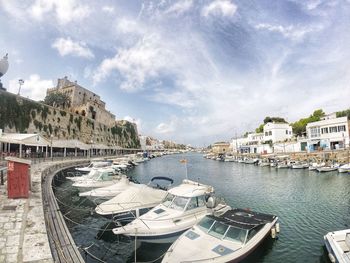 Boats moored in river by buildings in city against sky