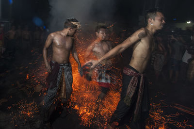 Shirtless men dancing on fire at night