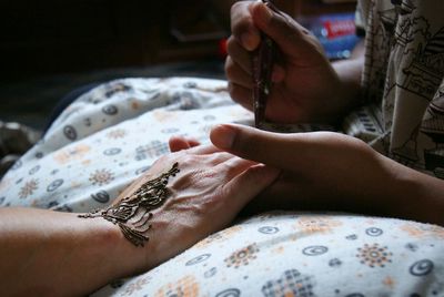 Cropped image of woman drawing henna tattoo on hand