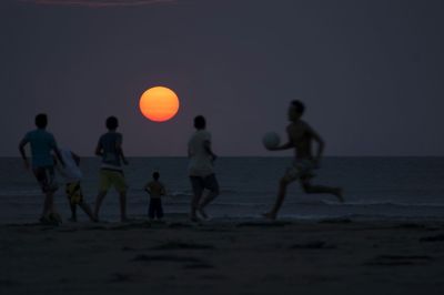 People playing on beach at sunset