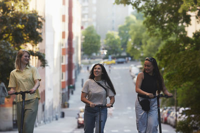 Young female friends riding electric push scooters in city