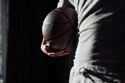 Midsection of man holding ball while standing against black background