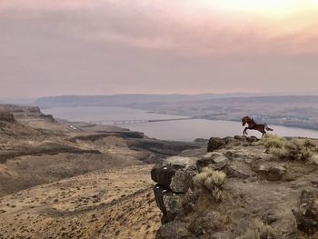 People riding motorcycle on land against sky during sunset