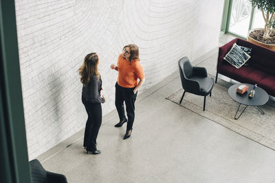 Businesswomen discussing while standing by wall at office