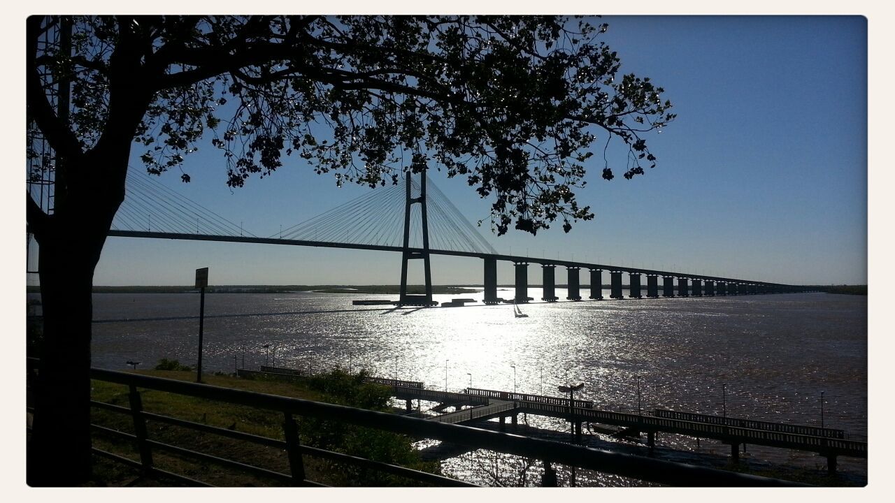 water, transfer print, connection, bridge - man made structure, bridge, auto post production filter, silhouette, railing, river, tranquility, tranquil scene, sea, tree, scenics, sky, clear sky, built structure, nature, beauty in nature, sunset