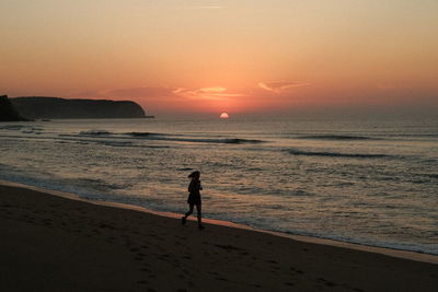 Silhouette of woman running on the beach during sunrise in portugal. shot on fujifilm x100v.