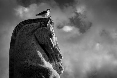 Low angle view of bird perching on statue against sky