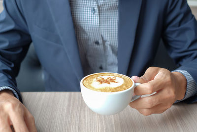 Midsection of man holding coffee cup on table