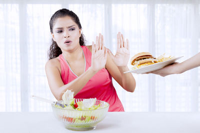 Woman with salad bowl refusing burger at home