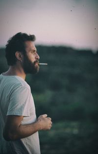 Side view of thoughtful man smoking cigarette while looking away outdoors