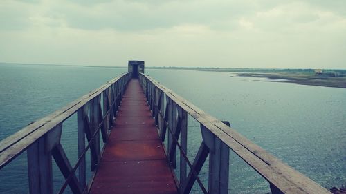 Empty pier on sea against cloudy sky