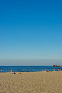 People on beach against clear blue sky