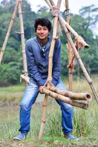 Full length portrait of young man sitting on bamboo over grass