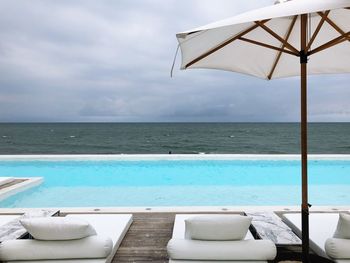 Lounge chairs on floorboard by sea against sky