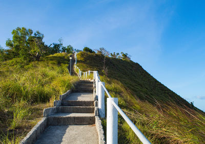 Staircase leading towards green landscape against blue sky