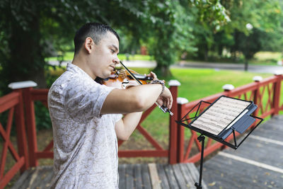 Violinist playing violin looking at sheet music in park