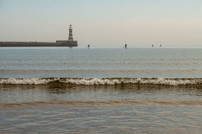 Lighthouse by sea against clear sky