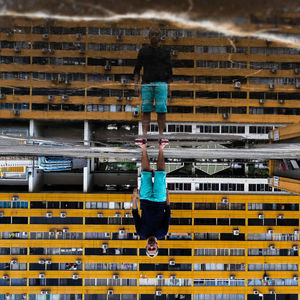 Reflection of man standing against building on puddle during rainy season