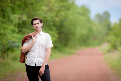 Portrait of young woman standing on road against trees