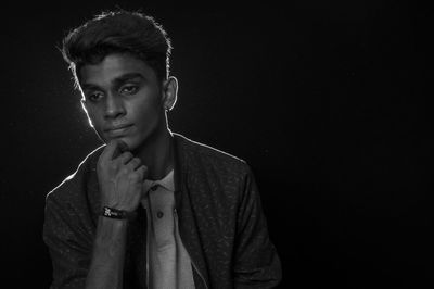 Thoughtful man with hand on chin looking away while standing in darkroom