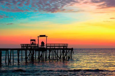 Silhouette people on pier over sea against sky during sunset