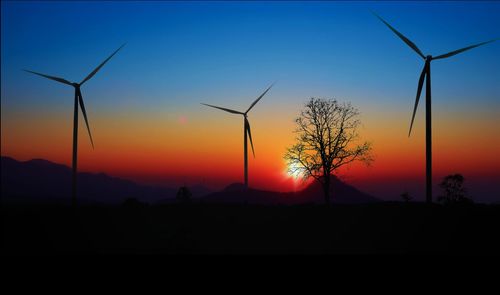 Silhouette of wind turbines against sky during sunset